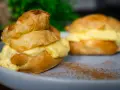 Zwei köstliche Windbeutel-Desserts, gefüllt mit cremiger Vanillecreme, auf einem Teller mit Zimt bestäubt.