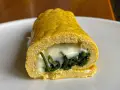 Rotolo di frittata dorato, ripieno di spinaci e formaggio filante, servito su un piatto bianco.