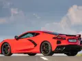 Czerwony Chevrolet Corvette C8 z czarnym spoilerem i felgami, zaparkowany na drodze pod błękitnym niebem z chmurami.