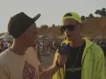 Dwóch mężczyzn na plaży, jeden z mikrofonem Red Bull, w tle tłum ludzi i scena.