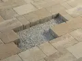 Fragment kostki brukowej z widocznym wycięciem i żwirem. Wiercenie w kostce brukowej jest w trakcie.