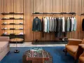 Eleganckie męskie ubrania wiszą na wieszakach, a na półkach wyeksponowane są koszule. Wnętrze emanuje cichym luksusem.