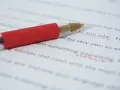 Czerwony długopis na białym papierze z zaznaczonymi błędami na czerwono.