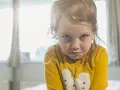 Mała dziewczynka w żółtej bluzce z misiem, z miną wyrażającą bunt 4 latka.