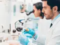 Ricerca di offerte di lavoro tecnico di laboratorio biomedico: due scienziati lavorano con provette e microscopio in un laboratorio moderno.