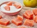 Leckeres Quittenbrot Rezept einfach: Süße, zuckerüberzogene Quittenstücke liegen auf Backpapier, daneben eine Schüssel mit Zucker und eine Quitte.