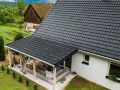 Nowy, czarny dach z blachodachówki nad tarasem i domem. Wymiana dachu zakończona sukcesem, dom zyskał nowy, nowoczesny wygląd.