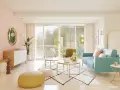 Un salón eclectico con sofá turquesa, mesa de centro dorada, pufs coloridos y un espejo ovalado.