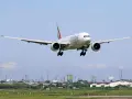 Emirates Boeing 777 zbliża się do lądowania. W tle widać przemysłowy krajobraz i inne samoloty na niebie, sugerujące ruch lotniczy, być może związane z dżerba loty.
