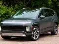Szary SUV Hyundai IONIQ 9 z charakterystycznym pasem świateł z przodu, na tle zieleni.