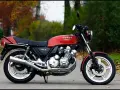Klasyczny czerwony motocykl Honda CBX 1000 z lat 80. stoi na drodze, otoczony jesienną zielenią i opadłymi liśćmi.