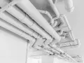 Skomplikowany system białych rur, przypominający pex, biegnie pod sufitem, tworząc geometryczny wzór.