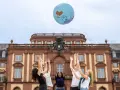 Studierende werfen einen Globus in die Luft vor dem Gebäude des akademischen Auslandsamtes.