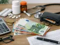 Kalkulator, pieniądze, leki i stetoskop sugerują analizę kosztów związanych ze zmianą ubezpieczenia w Holandii.