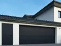 Nowoczesne, czarne drzwi do garażu wewnętrzne i przylegające do nich drzwi wejściowe do budynku, pod ciemnym dachem.