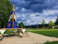Spielplatz am Badesee Ludwigsburg mit Segel-Klettergerüst und Sandkasten. Im Hintergrund der See und Menschen.