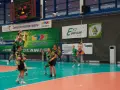 Mecz siatkówki w Zawierciu. Zawodnicy w zielonych strojach walczą o piłkę pod koszem.