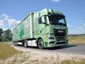Zielona ciężarówka MAN TGX z naczepą TIP jedzie drogą. Na naczepie widnieje napis "Ucz się z najlepszymi!".