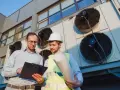 Dwóch inżynierów analizuje dokumentację techniczną przy wielkich wentylatorach. To ich świadectwo ATP, że wszystko działa poprawnie.