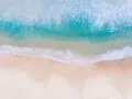 Vue aérienne d'une photo à la plage, avec des vagues turquoise déferlant sur le sable doré.