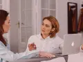 Dos mujeres discuten un traspaso de negocio en funcionamiento. Una tiene un portátil abierto.