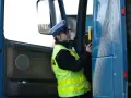 Policjantka w kamizelce odblaskowej i czapce przykłada alkomat do drzwi ciężarówki.