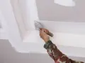Mano con espátula aplica masilla para pegar escayola rota en el techo.