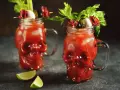 Dwa krwawe drinki ze spirytusem w szklankach w kształcie czaszek, udekorowane łodygami selera, oliwkami i plasterkami salami.