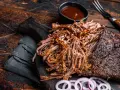 Soczysta, aromatyczna szarpana wołowina, polana sosem BBQ, podana z krążkami cebuli na drewnianej desce. Idealna na grilla.