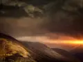 Dramatic sunburst pierces dark clouds over a rugged mountain range, a powerful display of the sovereignty of God.