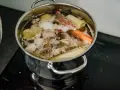 Gotuje się mętny rosół z kurczaka z warzywami i przyprawami.