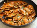 Mejillones con tomate en salsa cremosa, espolvoreados con perejil fresco, servidos en una sartén negra.