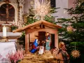 Weihnachtskrippe in einer Kirche, die die Geburt Jesu darstellt. Maria und Josef knien vor dem Kind, während im Hintergrund ein Weihnachtsbaum und Kerzen leuchten. So feiert man Weihnachten.