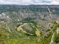 Vue aérienne du cirque de Navacelles, un méandre de rivière creusé dans un paysage de garrigue et de falaises calcaires, avec un village niché au fond.