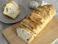 Pyszny chlebek czosnkowy rwany, idealny do dzielenia się. Obok dwa ząbki czosnku i kromki chleba na talerzyku.