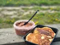 Färdiga proteinpannkakor i en svart behållare bredvid en burk med chokladpålägg, redo att avnjutas utomhus.