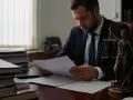 Prawnik analizuje dokumenty, rozważając przedawnienie długu. Obok stoi Temida.