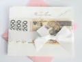Elegancka koperta z banknotami 200 zł, przewiązana białą wstążką. Idealny prezent ślubny, choć warto pamiętać o potencjalnym podatku od prezentów ślubnych.