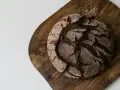 Chleb bez mąki, ciemny, okrągły bochenek z popękaną skórką, leży na drewnianej desce.