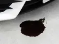 Wyciek oleju z silnika na betonowej nawierzchni. Ciemna plama oleju pod przednią częścią białego samochodu.