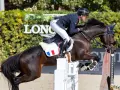 Cavalier français en plein saut lors d'un concours hippique. Le cheval, puissant et concentré, franchit un obstacle blanc.