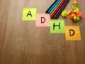 Kolorowe karteczki z literami "A", "D", "H", "D" układają się w napis ADHD. Obok leżą pisaki i pomięte papierki, jakby ktoś próbował znaleźć rozwiązanie, może z pomocą leku Elvanse.