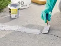 Applying pre-mixed concrete patch to fix cracks in pavement. A gloved hand uses a trowel to smooth the patch.