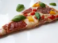Kawałek pysznej pizzy keto z salami, papryką i bazylią na białym talerzu.