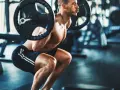 Man gör ett tungt benspark hemma med skivstång på axlarna i ett gym.