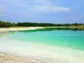 Lazurowe jezioro o turkusowej barwie, z piaszczystym brzegiem i odbijającym się w wodzie zielonym lasem.