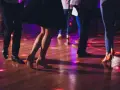 Ludzie tańczą w rytm znanych piosenek, tworząc widowiskowe układy taneczne. Kolorowe światła odbijają się od parkietu.