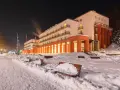 Zimowy wieczór w sanatorium godnym polecenia. Ośnieżone ławki i oświetlony budynek zapraszają do odpoczynku.