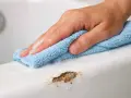 Main d'une personne nettoyant une rayure sur une baignoire en acrylique avec un chiffon bleu.