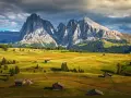 Un paesaggio alpino con un sasso lungo e imponente che domina un sasso piatto e verdeggiante, punteggiato da casette di legno.